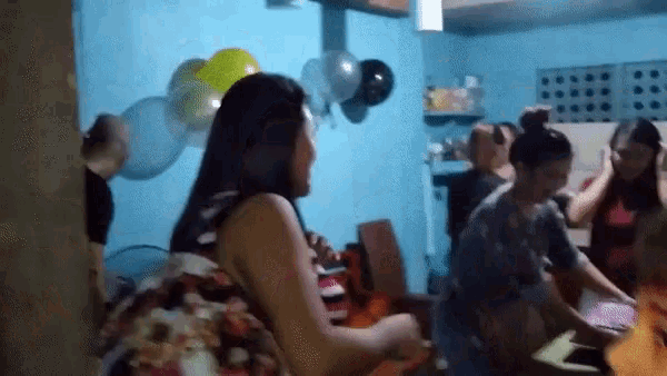 a group of people are gathered in a room with balloons on the walls