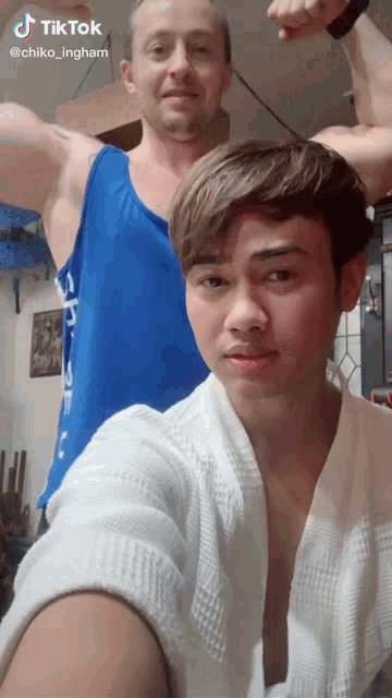 a man in a blue tank top is flexing his muscles next to a young man in a white robe ..