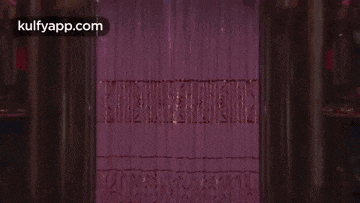 a man and a woman are dancing in front of a purple curtain .
