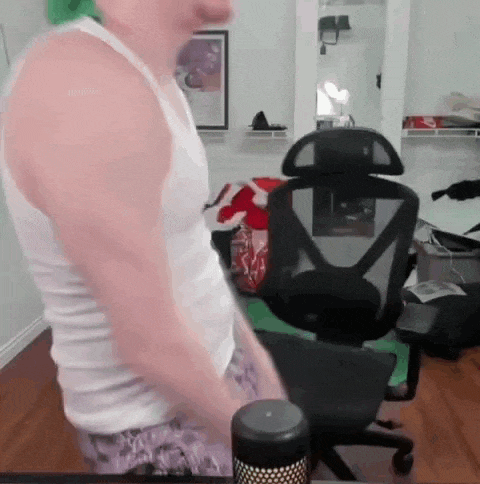 a man in a white tank top is standing in front of a computer chair .