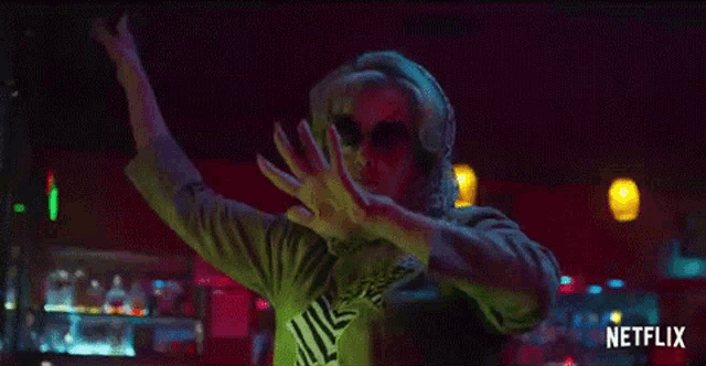 a woman wearing sunglasses and headphones is dancing in a dark room .