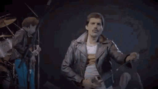 a man in a leather jacket is playing a guitar on a stage in front of drums .