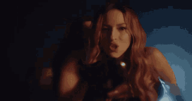 a woman with red hair is holding a gun in a dark room while another woman looks on .