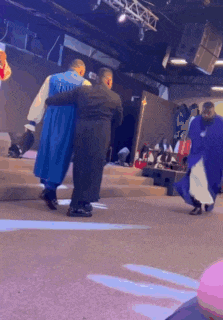 a group of men are standing on a stage in a church . one of the men is wearing a blue cape .