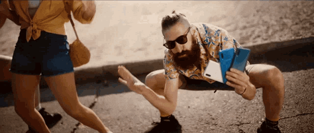 a man with a beard is squatting down while holding a cellphone