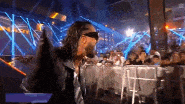 a wrestler wearing sunglasses is standing in front of a crowd .