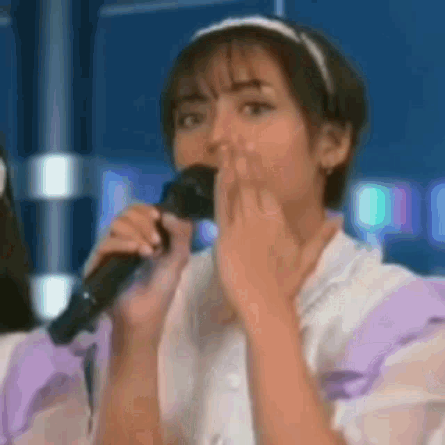 a woman is singing into a microphone while covering her mouth .