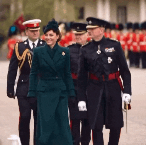 a woman in a green coat is walking with a group of men in uniforms