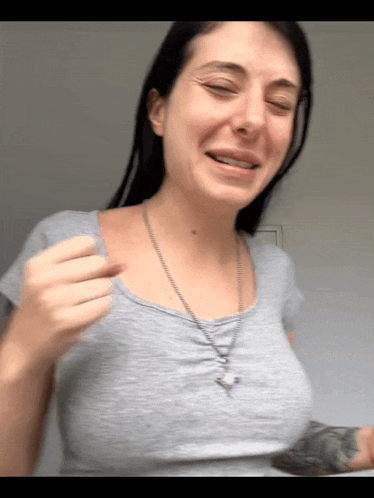 a woman wearing a grey t-shirt and a necklace is smiling
