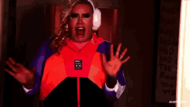 a drag queen wearing headphones and an orange jacket is screaming .