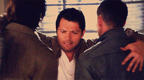 three men are hugging each other in a room and one of them is looking at the camera .