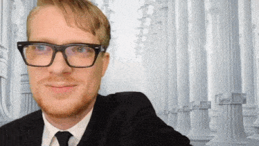 a man wearing glasses and a suit is smiling in front of columns