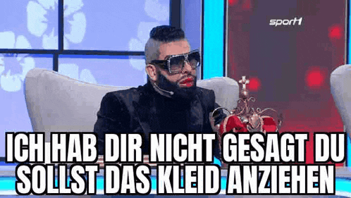 a man with a beard and sunglasses is sitting in a chair with a microphone .