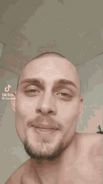 a shirtless man with a shaved head and a beard is smiling with his eyes closed ..