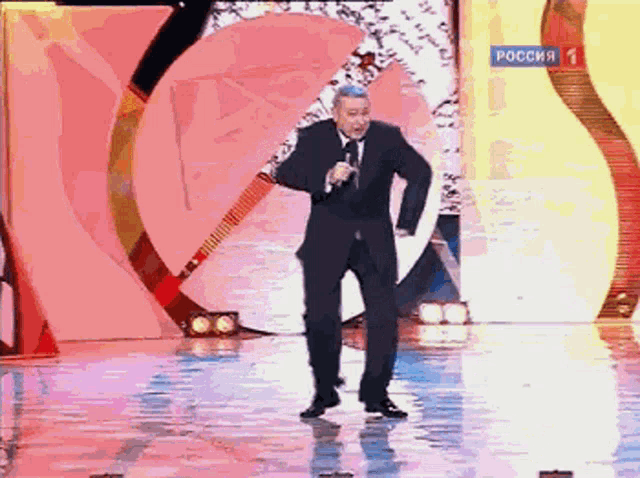a man in a suit and tie stands on a stage with a microphone and a sign that says " russia "