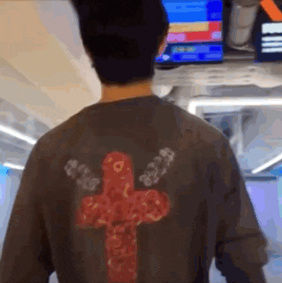 a man wearing a shirt with a red cross on the back is standing in front of a television .