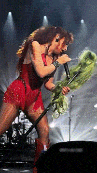 a woman singing into a microphone with a green wig