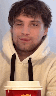 a man in a white hoodie is holding a red cup of coffee .