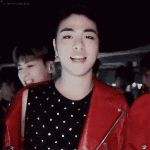 a young man wearing a red leather jacket and a black and white polka dot shirt is smiling .