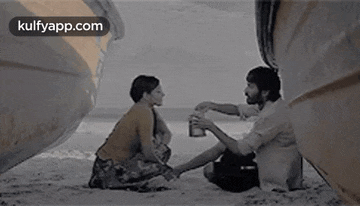 a man and a woman are sitting on the beach next to a boat .