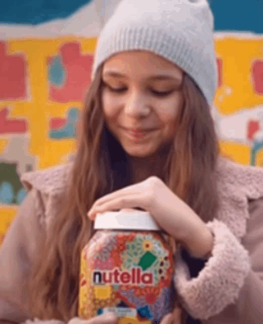 a girl is holding a jar of nutella and smiling .