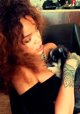 a woman with a tattoo on her arm is holding a small black dog