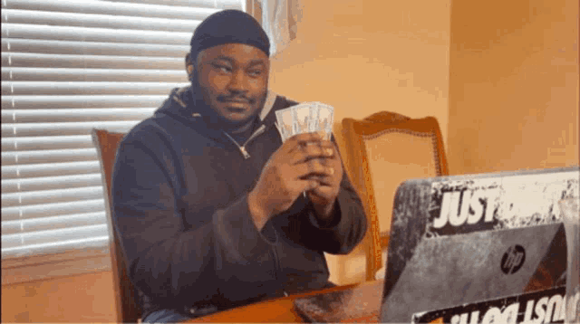 a man sitting at a table with a laptop that has a just do it sticker on it