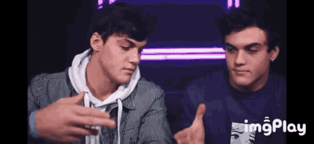 two young men are sitting next to each other in front of purple lights .
