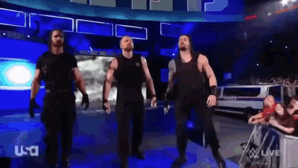 a group of wrestlers are walking on a stage in front of a crowd while wearing black shirts .