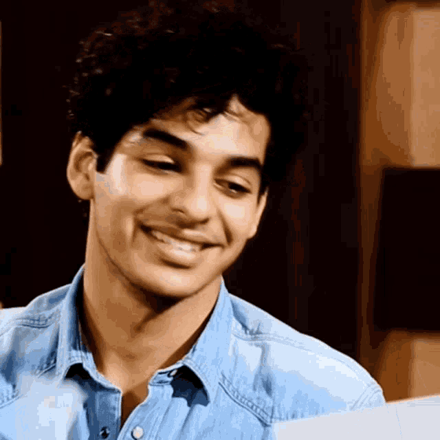 a young man wearing a blue denim shirt is smiling and looking down .