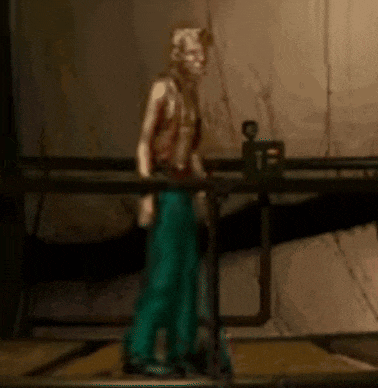 a statue of a man in a brown vest and green pants is standing next to a table .