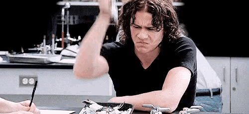 a man with curly hair is sitting at a table with a plate of food and a fork .