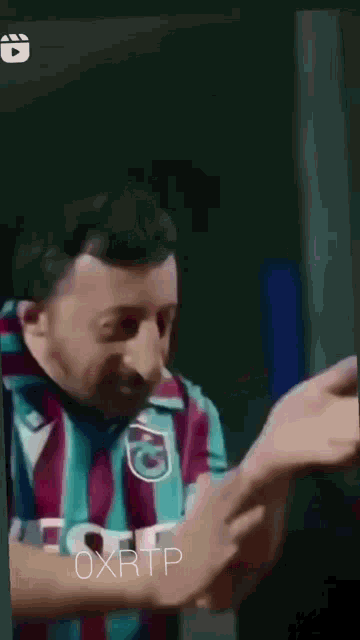 a man with a beard is wearing a striped shirt and scarf and making a funny face .