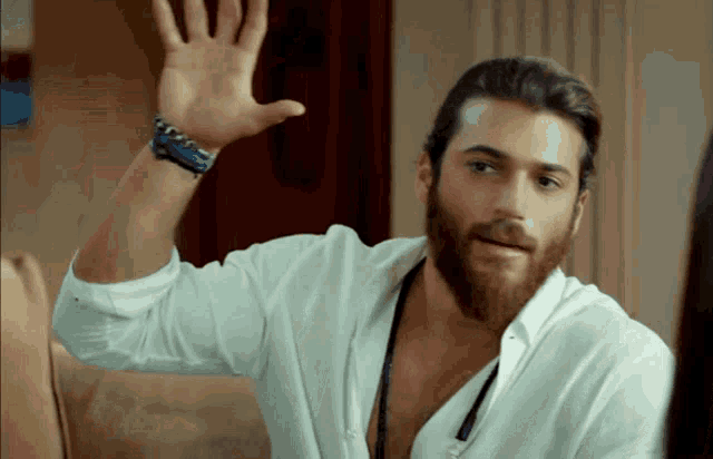 a man with a beard wearing a white shirt is waving