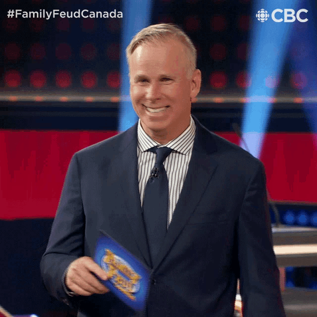 a man in a suit and tie is smiling while holding a clipboard with the words family feud canada on the bottom