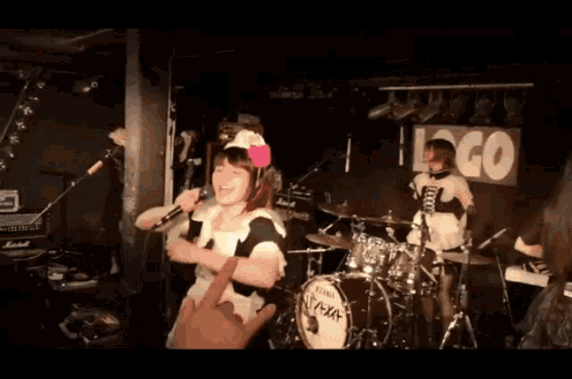 a woman singing into a microphone in front of a drum set with a sign that says " go "