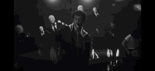 a man is singing into a microphone on a stage while a band plays behind him .