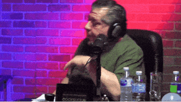 a man wearing headphones talks into a microphone in front of a sign that says cocksucka !
