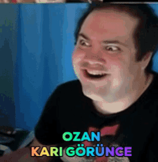 a man in a black shirt is smiling with the words ozan kari gorunce written above him