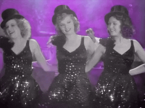 three women in sequined dresses and top hats are dancing in a black and white photo .