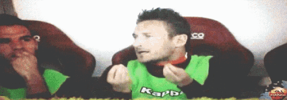 a man wearing a green kappa shirt is sitting in a red chair