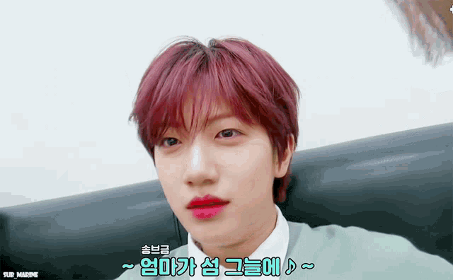 a young man with red hair is sitting on a couch with korean writing around his face