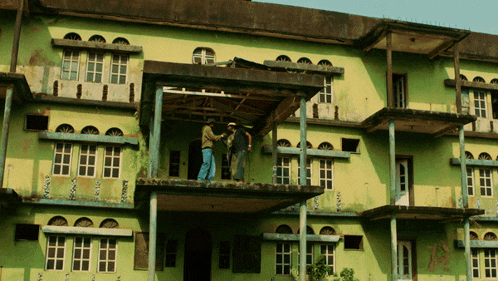 two men stand on a balcony of a green building