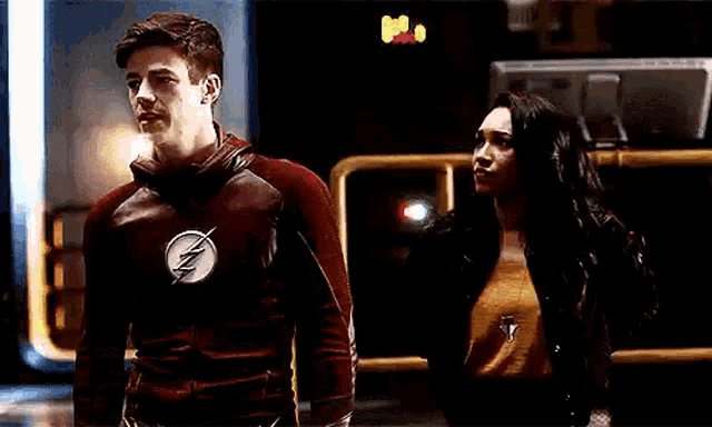 a man in a flash suit and a woman in a black jacket are standing next to each other in a dark room .