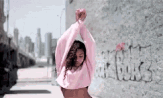 a woman in a pink crop top is dancing in front of a wall with graffiti on it