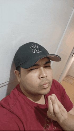 a man wearing a ny hat and a red shirt is making a face