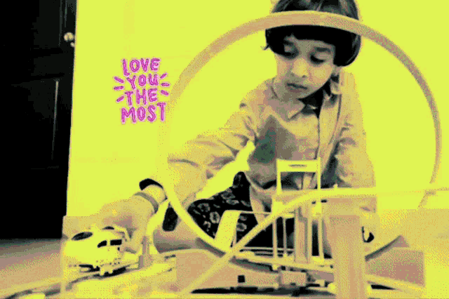 a child is playing with a toy train set with a yellow background that says love you the most on it