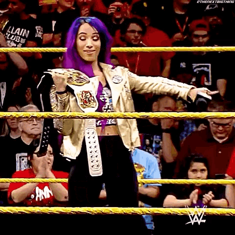 a woman with purple hair is standing in a wrestling ring with a belt around her waist .