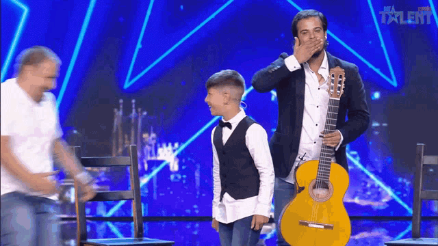 a man covering his mouth with his hand while holding a guitar on a stage