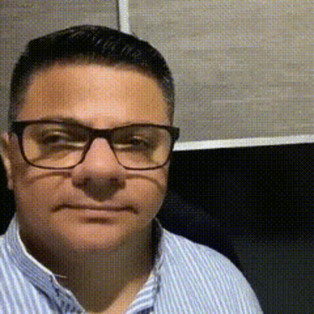 a man wearing glasses and a striped shirt looks at the camera
